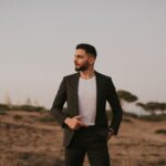 Man in suit posing confidently in a serene desert landscape at dusk.